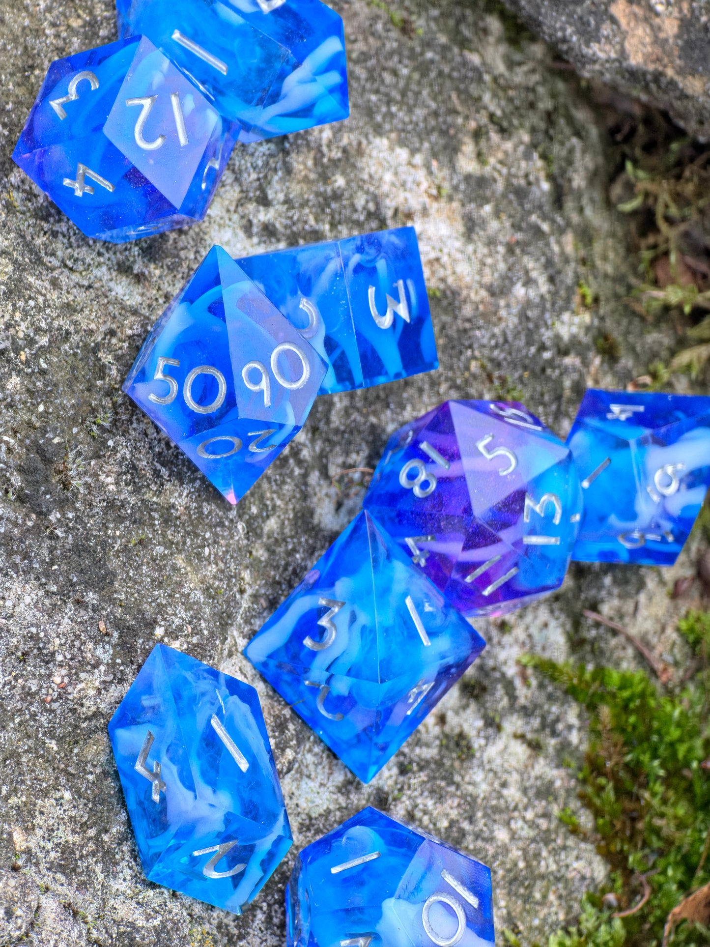 Handgemachtes Galaxy-DnD-Würfelset in leuchtendem Blau mit feinem Lila-Glanz, aufgenommen auf grauem Stein.