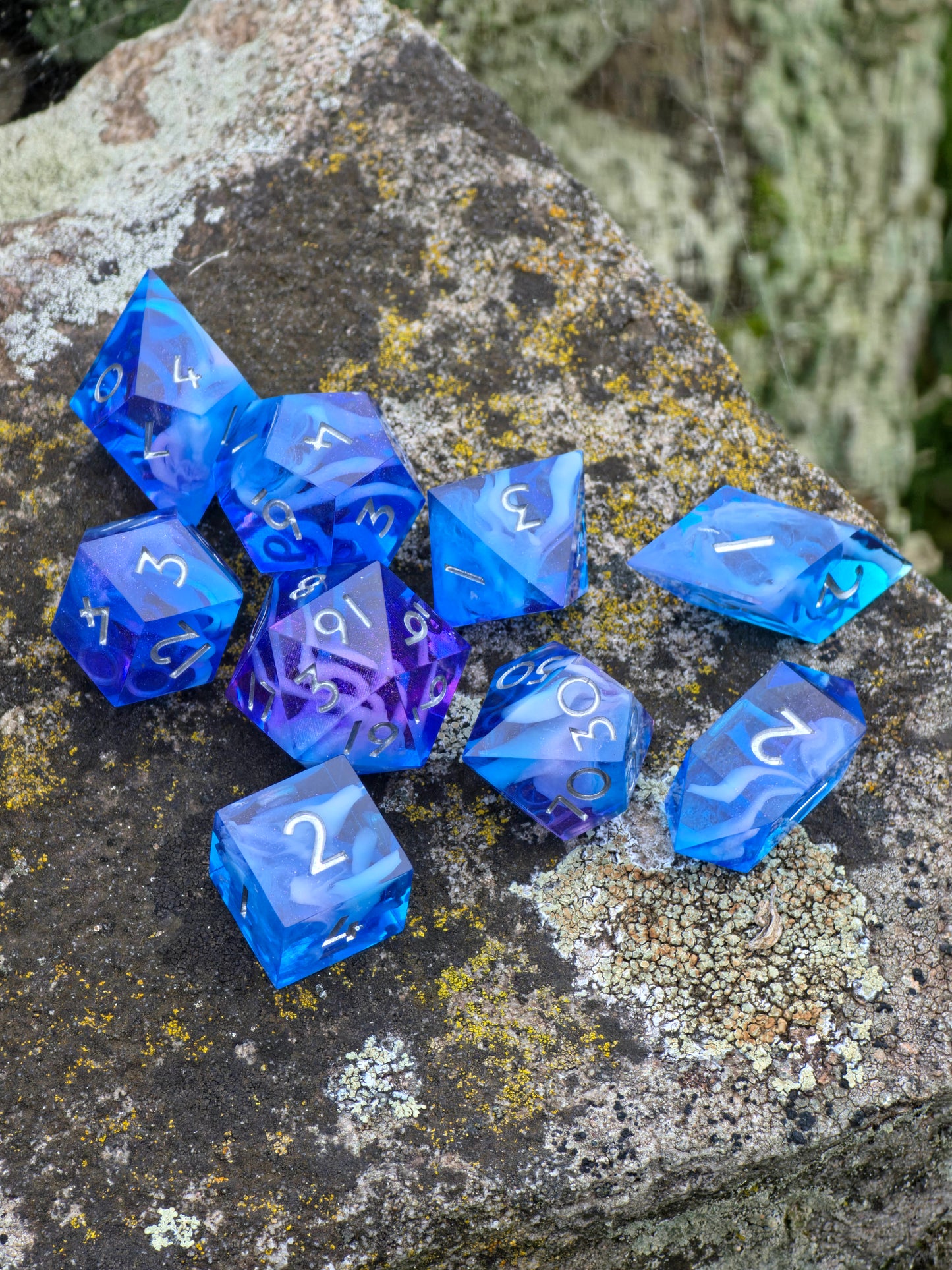 Nahaufnahme eines handgemachten Cloud Nebula Dice Sets in Blau mit sanftem lila Schimmer, auf Stein platziert.