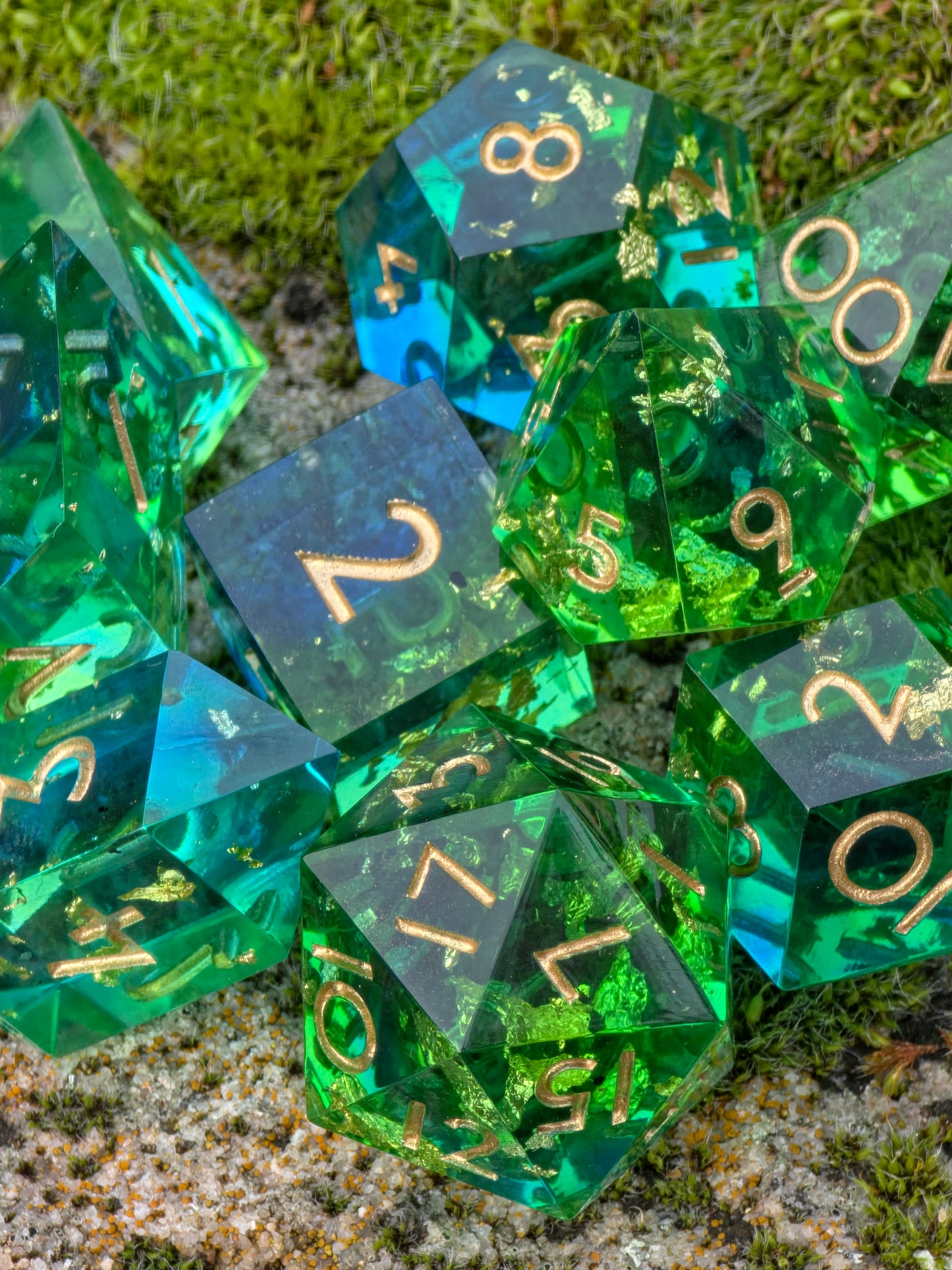 Transparente grün-blaue Resin-Würfel mit goldenen Flakes aus dem „Emerald Tide“ Set, auf Stein fotografiert.
Transparent green-blue resin dice with gold flakes from the “Emerald Tide” set, photographed on stone.