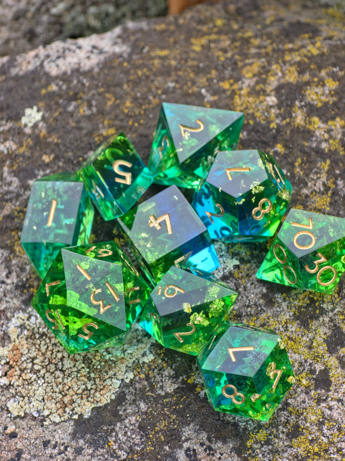 „Emerald Tide“ Würfelset auf Moos arrangiert – grün-blau transparent mit goldenen Flakes.
“Emerald Tide” dice set arranged on moss – green-blue transparent with gold flakes.