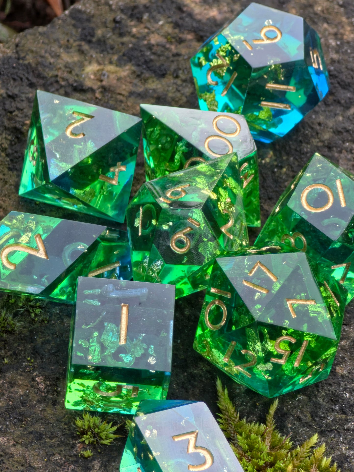 Nahaufnahme des polyedrischen „Emerald Tide“ Würfelsets in Grün und Blau mit feinen Goldflakes auf grauem Hintergrund.
Close-up of the polyhedral “Emerald Tide” dice set in green and blue with fine gold flakes on a grey background.