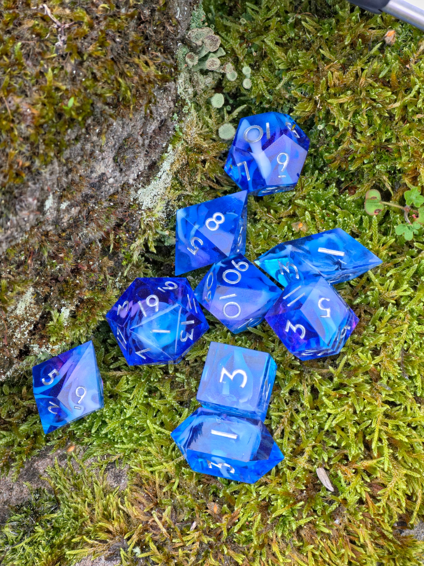 Handgemachtes Galaxy-DnD-Würfelset in leuchtendem Blau mit feinem Lila-Glanz, aufgenommen auf grauem Stein.