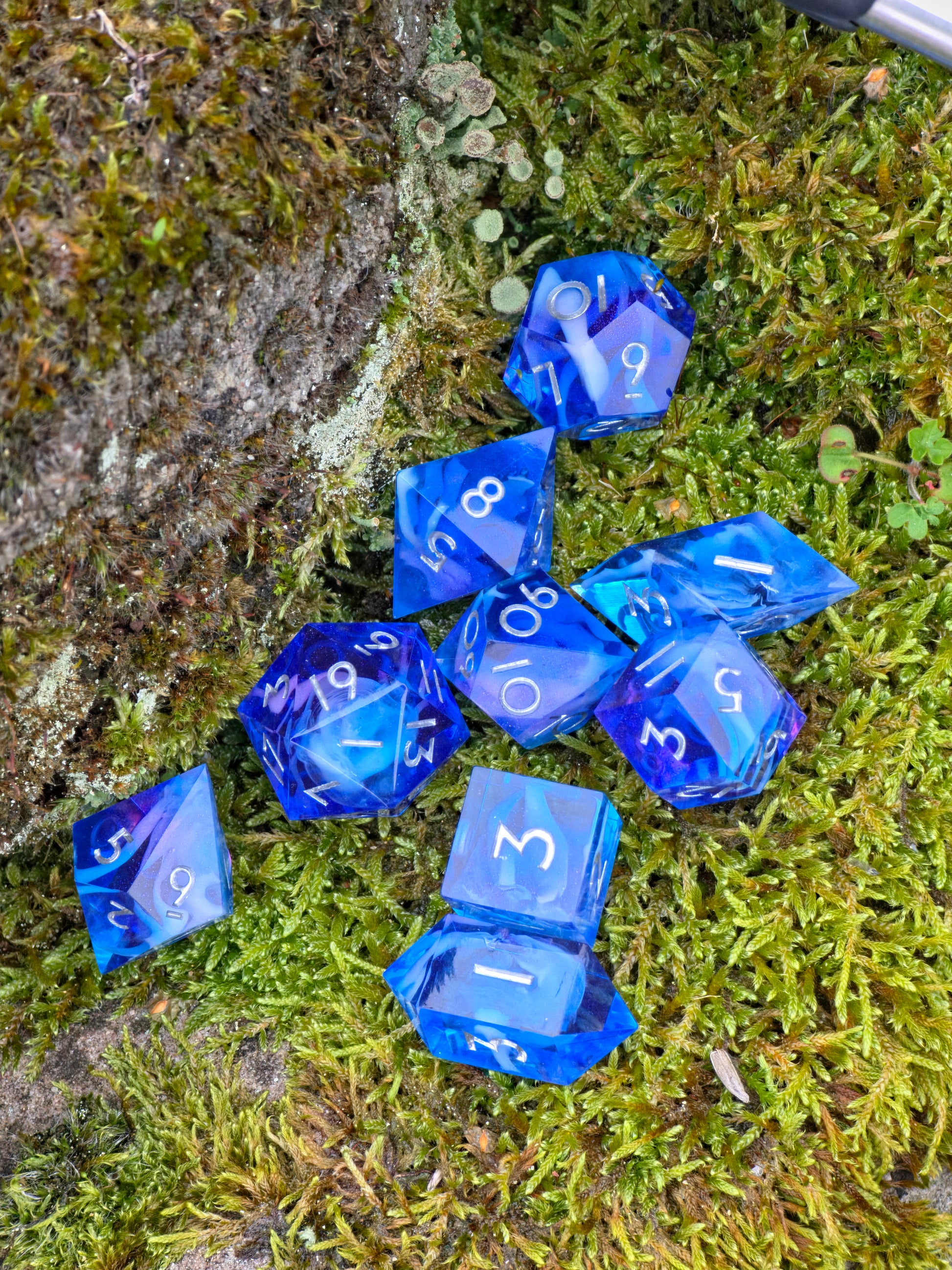 Handgemachtes Galaxy-DnD-Würfelset in leuchtendem Blau mit feinem Lila-Glanz, aufgenommen auf grauem Stein.