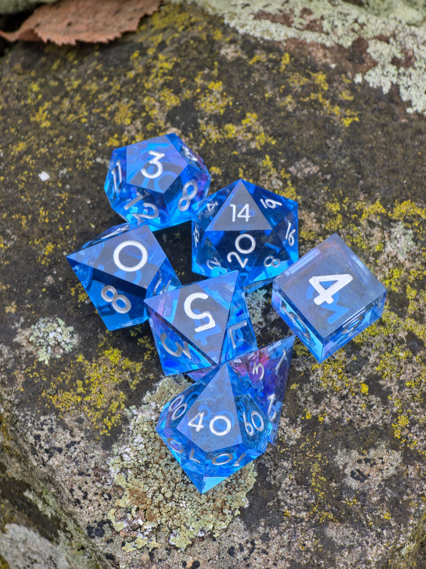Abyss of the Sapphire Tide“ Würfelset im natürlichen Licht, leuchtendes Saphirblau mit transparenter Klarheit.  
Abyss of the Sapphire Tide” dice set in natural light, glowing sapphire blue with crystal-clear transparency.