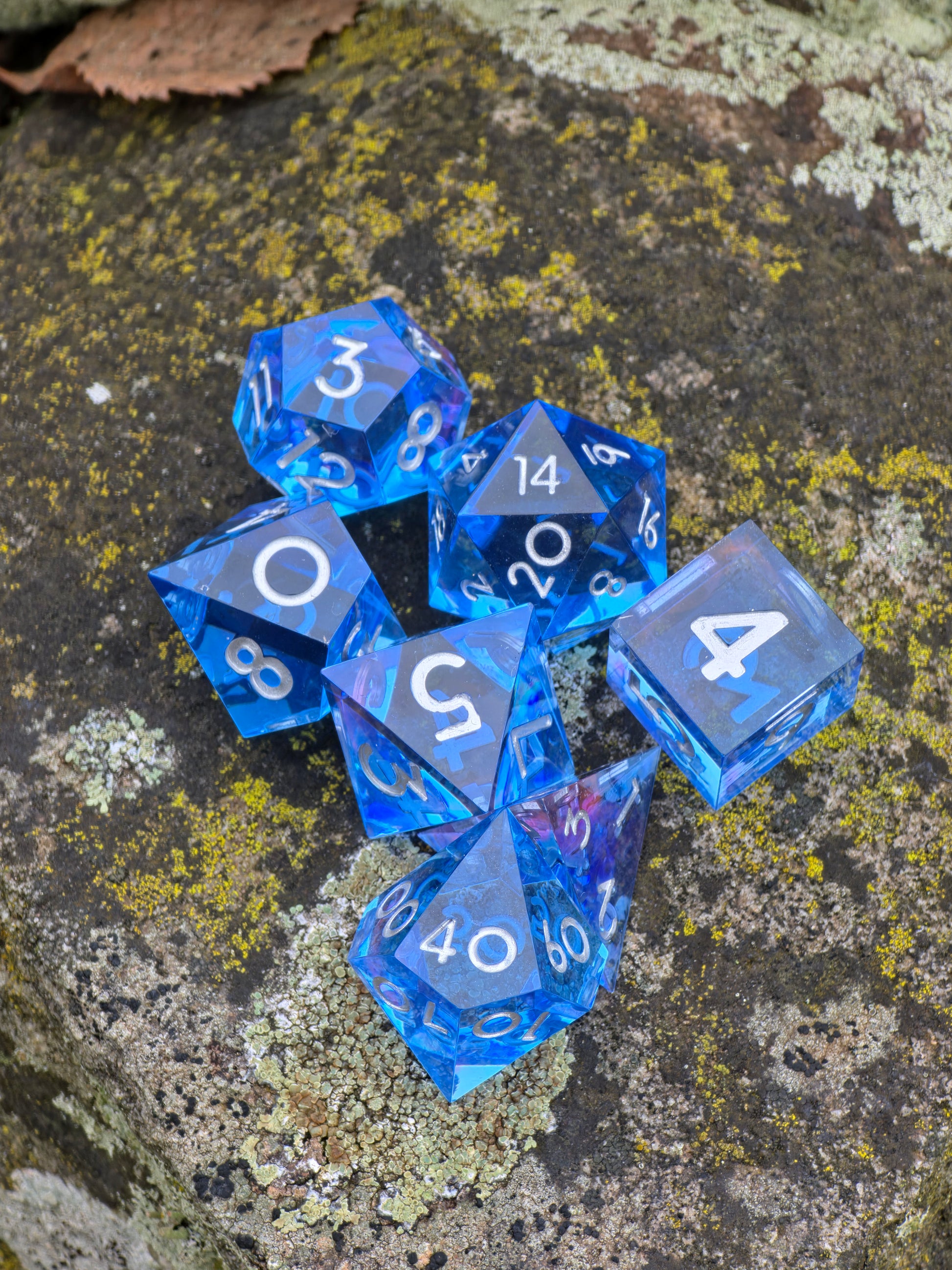 Abyss of the Sapphire Tide“ Würfelset im natürlichen Licht, leuchtendes Saphirblau mit transparenter Klarheit.  
Abyss of the Sapphire Tide” dice set in natural light, glowing sapphire blue with crystal-clear transparency.