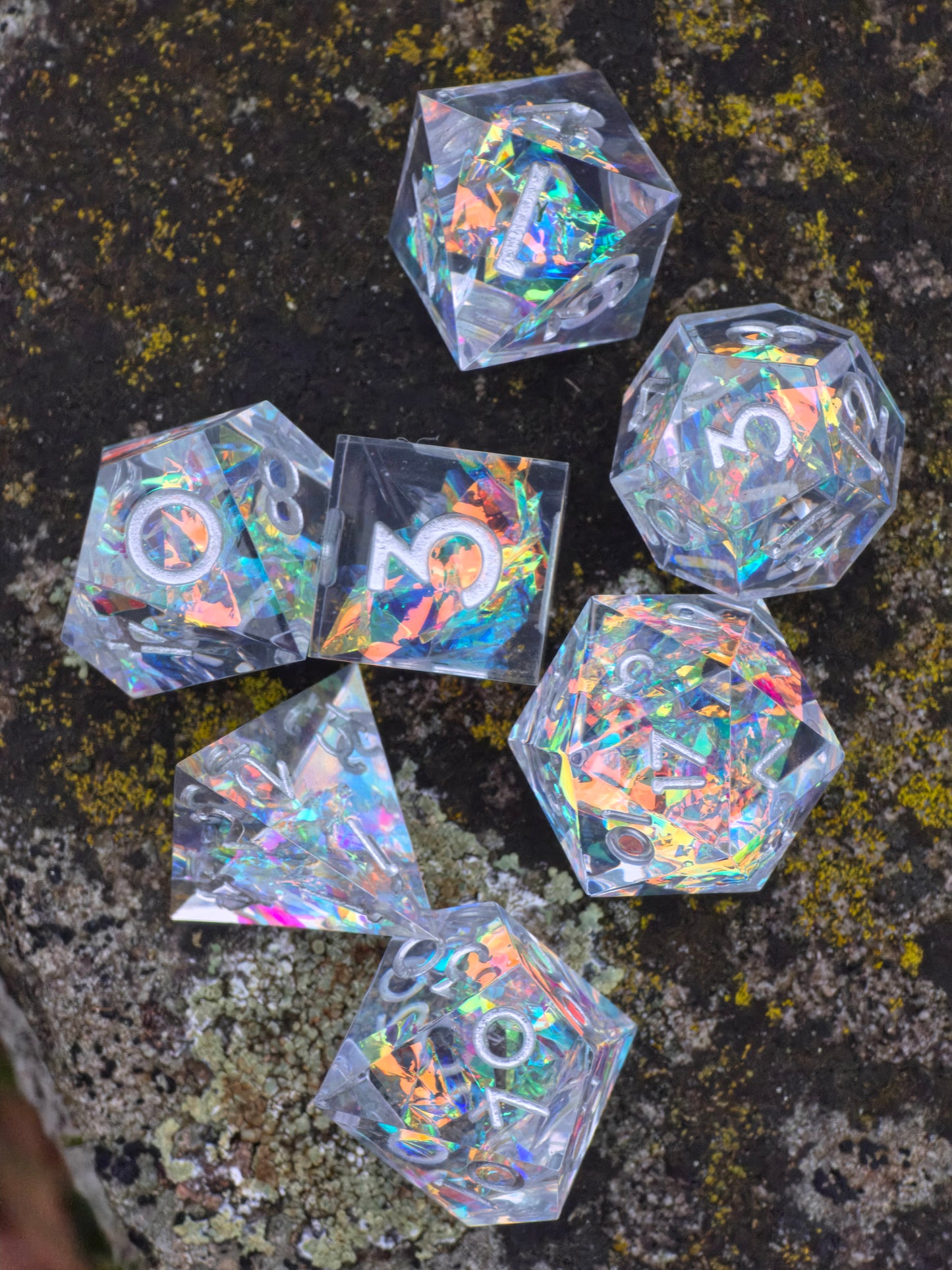 Aether Shards Würfelset im Freien – klare polyedrische Würfel mit holografischem Kristallschimmer. 
Aether Shards dice set outdoors – clear polyhedral dice with holographic crystal shimmer.