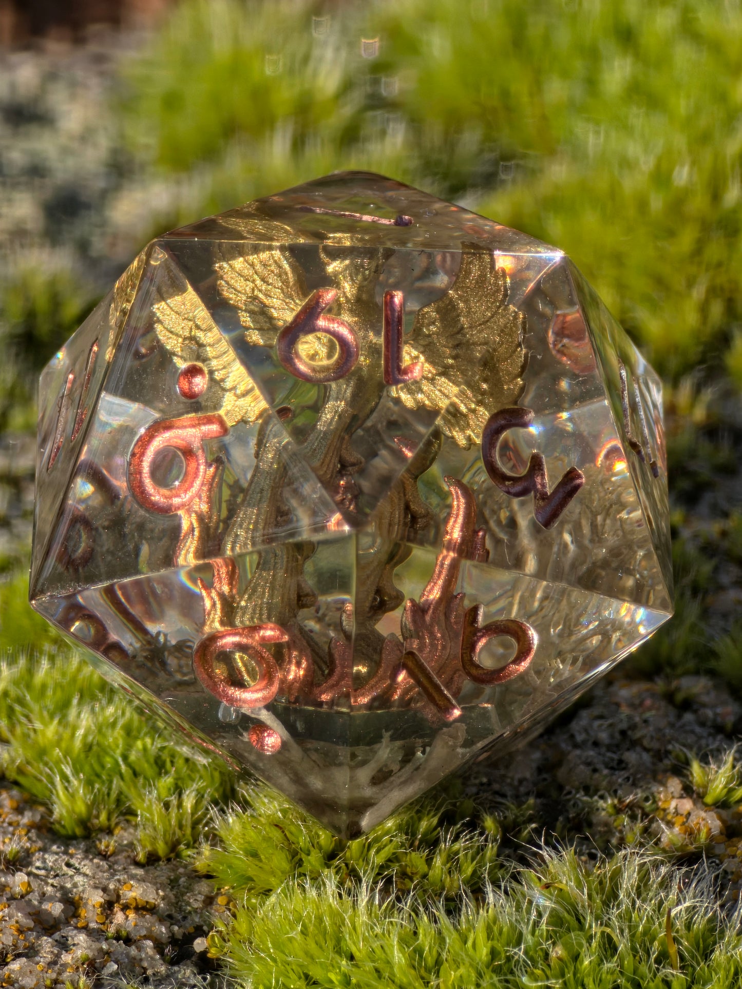 Aschekrone goldener Phönix D20 (28 mm) in der Hand zur Darstellung von Größe, Tiefe und Transparenz.  
Aschekrone golden phoenix D20 (28 mm) shown in hand to display size, depth and transparency.