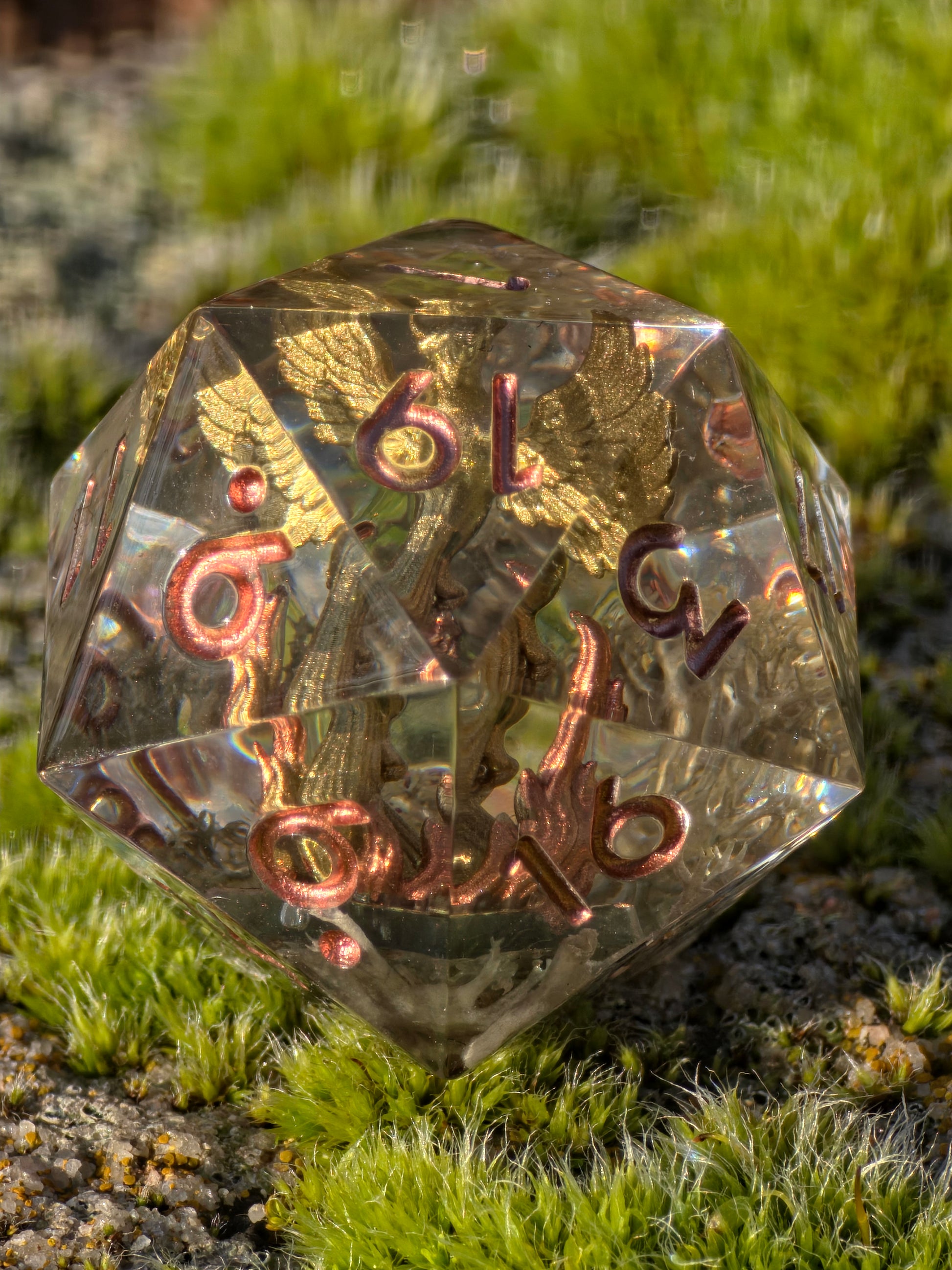 Aschekrone goldener Phönix D20 (28 mm) in der Hand zur Darstellung von Größe, Tiefe und Transparenz.  
Aschekrone golden phoenix D20 (28 mm) shown in hand to display size, depth and transparency.