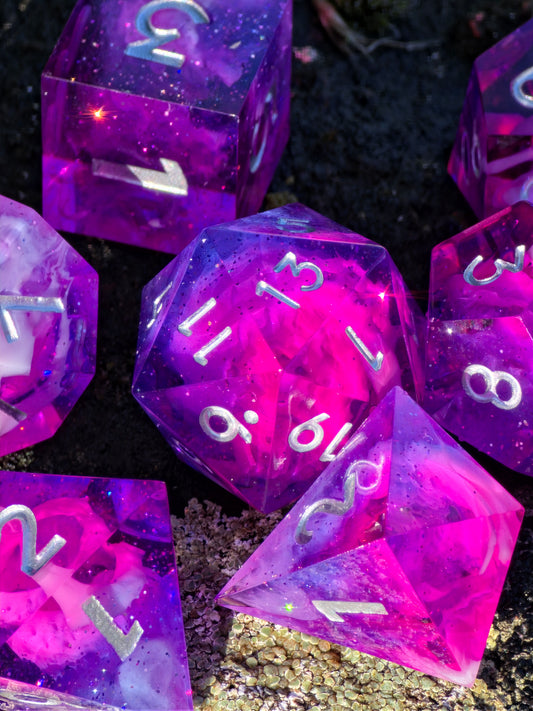 „Astral Bloom Nebula“ – pink-violettes polyedrisches Würfelset mit Galaxy- und Cloud-Effekt sowie weißen Zahlen.  
“Astral Bloom Nebula” – pink-purple polyhedral dice set with galaxy and cloud effects and white numbers.