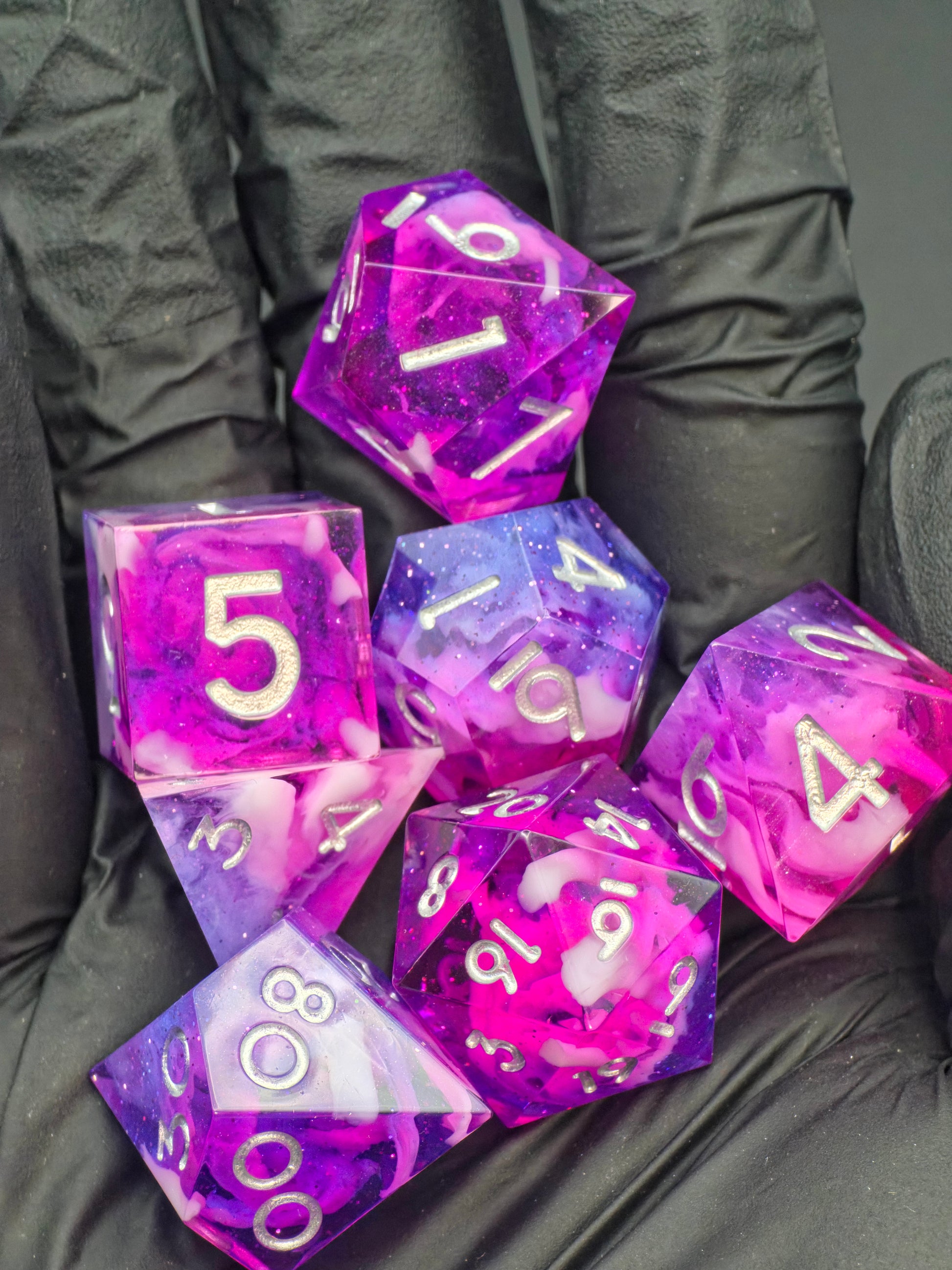 Galerieansicht des „Astral Orchard“ Würfelsets aus verschiedenen Perspektiven, rosa-violett mit silbernen Zahlen.  
Gallery view of the “Astral Orchard” dice set from multiple angles, pink-purple with silver numbers.