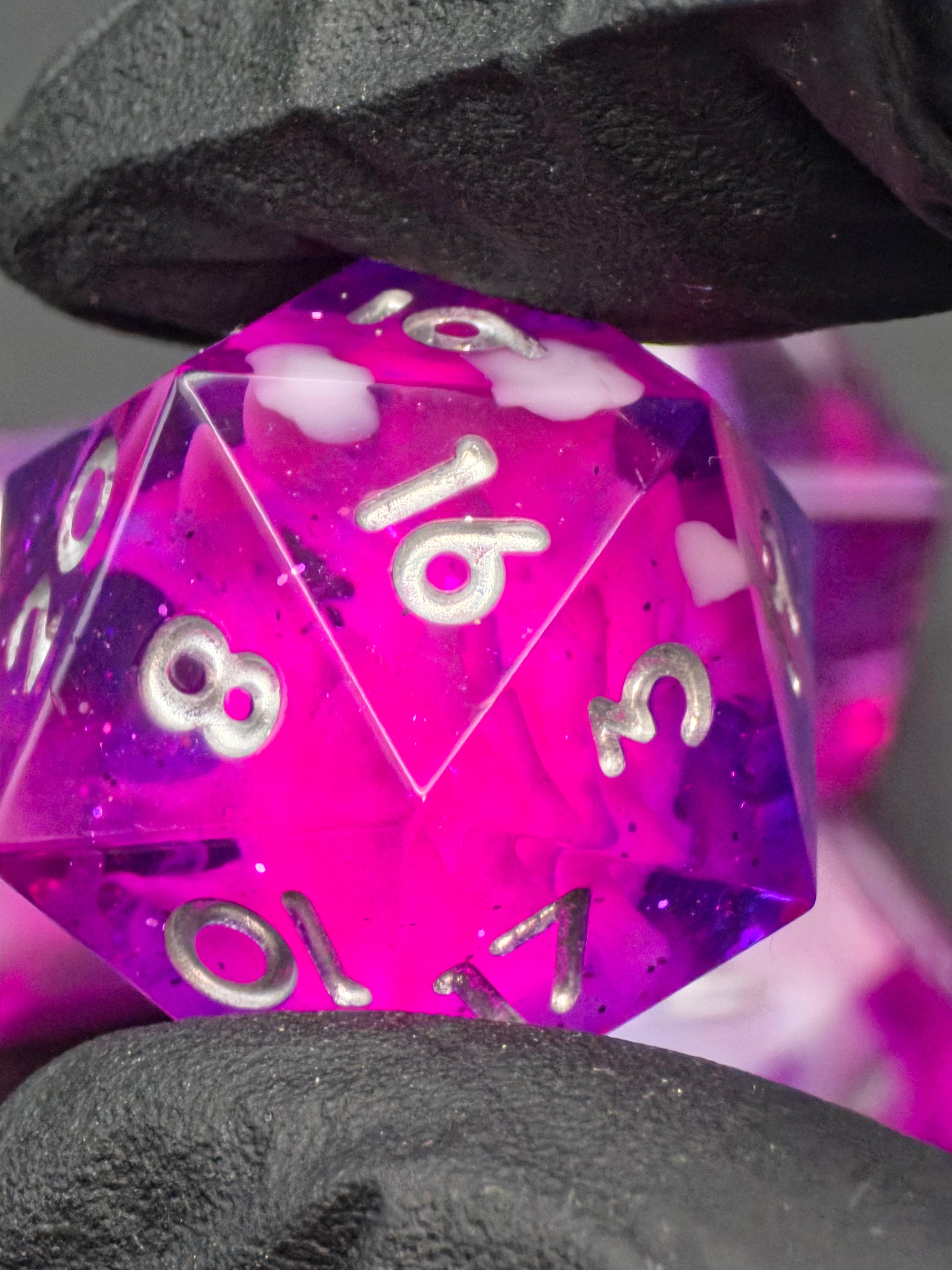 Handaufnahme des „Astral Orchard“ Würfelsets, violett-rosa Resinwürfel in Standardgröße für DnD und TTRPG.  
Hand shot of the “Astral Orchard” dice set, purple-pink resin dice in standard size for DnD and TTRPG.