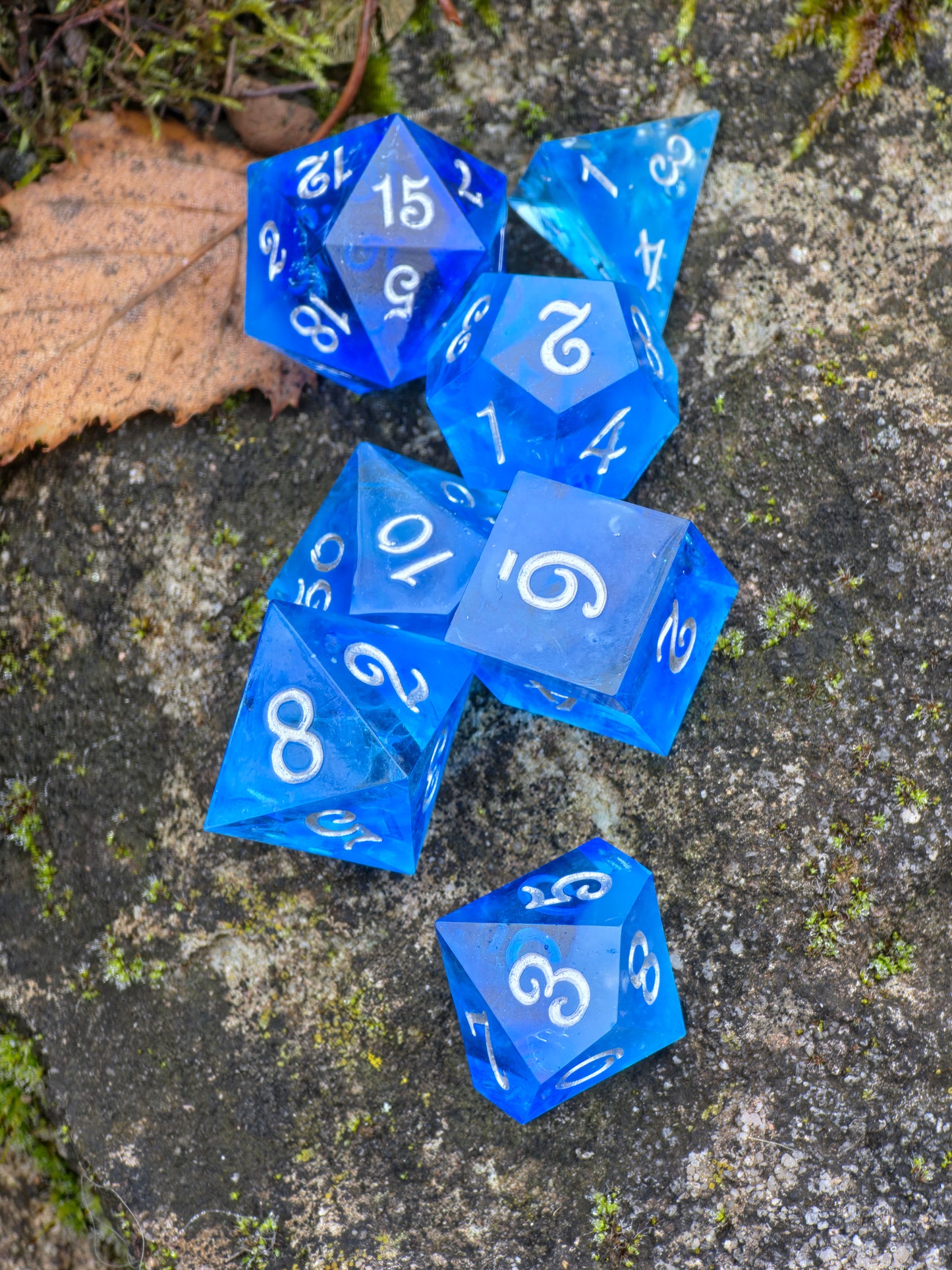 Blue glow-in-the-dark nebula resin dice set with silver numbers, sharp edges, photographed on natural stone