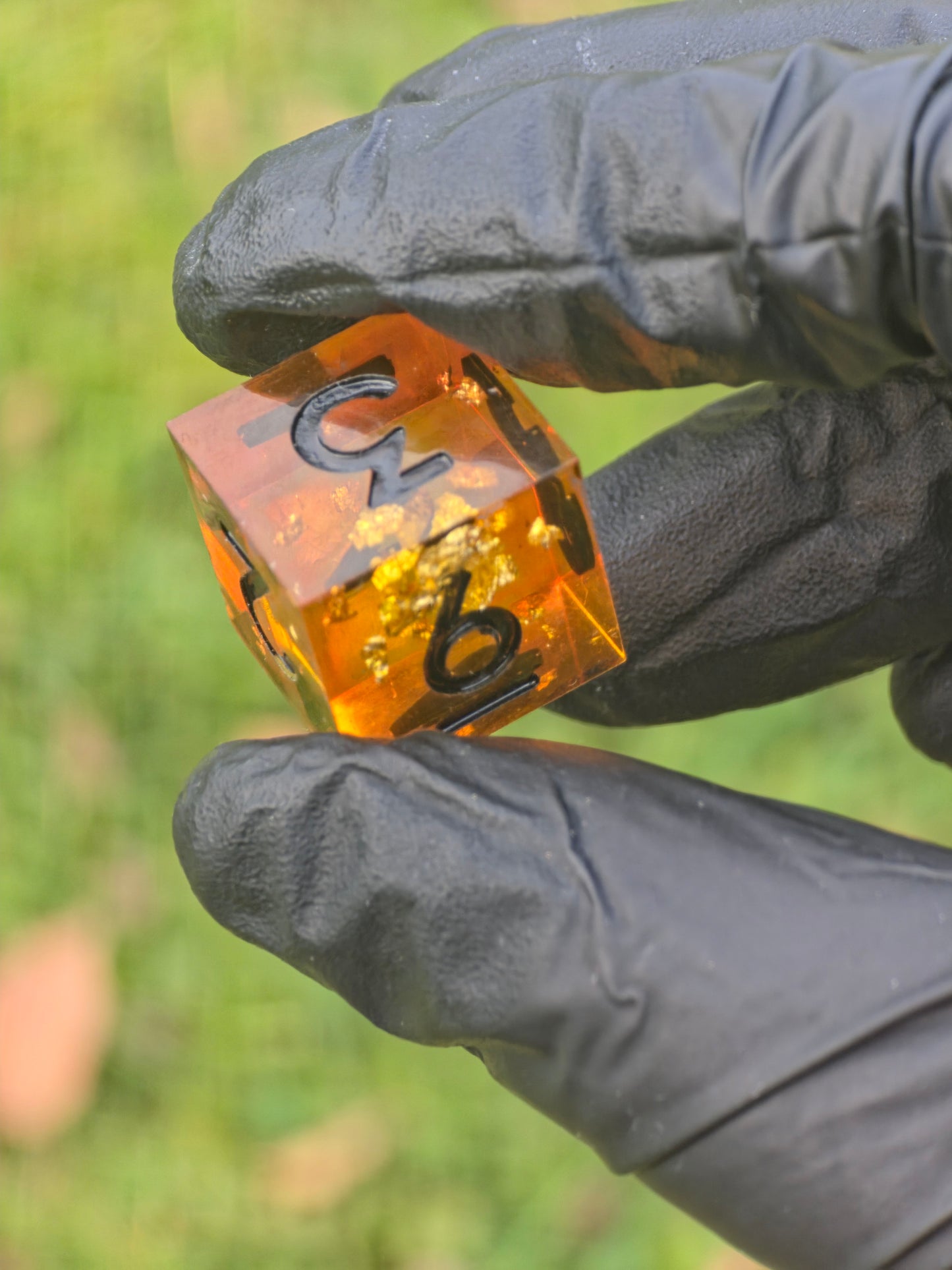 D6 „Bernstein Fragment“ – Seitenansicht des amber-orangenen Würfels mit schimmernden Goldflakes.  
Amber Fragment D6 – side view of the amber-orange die with shimmering gold flakes.