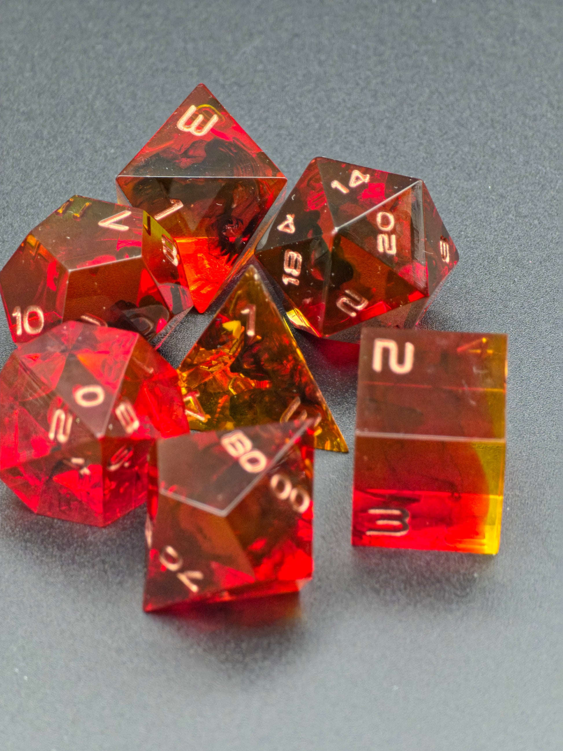 „Crimson Emberflow“ Würfelset im natürlichen Licht, leuchtende Feuer- und Bernsteintöne.  
“Crimson Emberflow” dice set in natural light, glowing fire-red and amber tones.