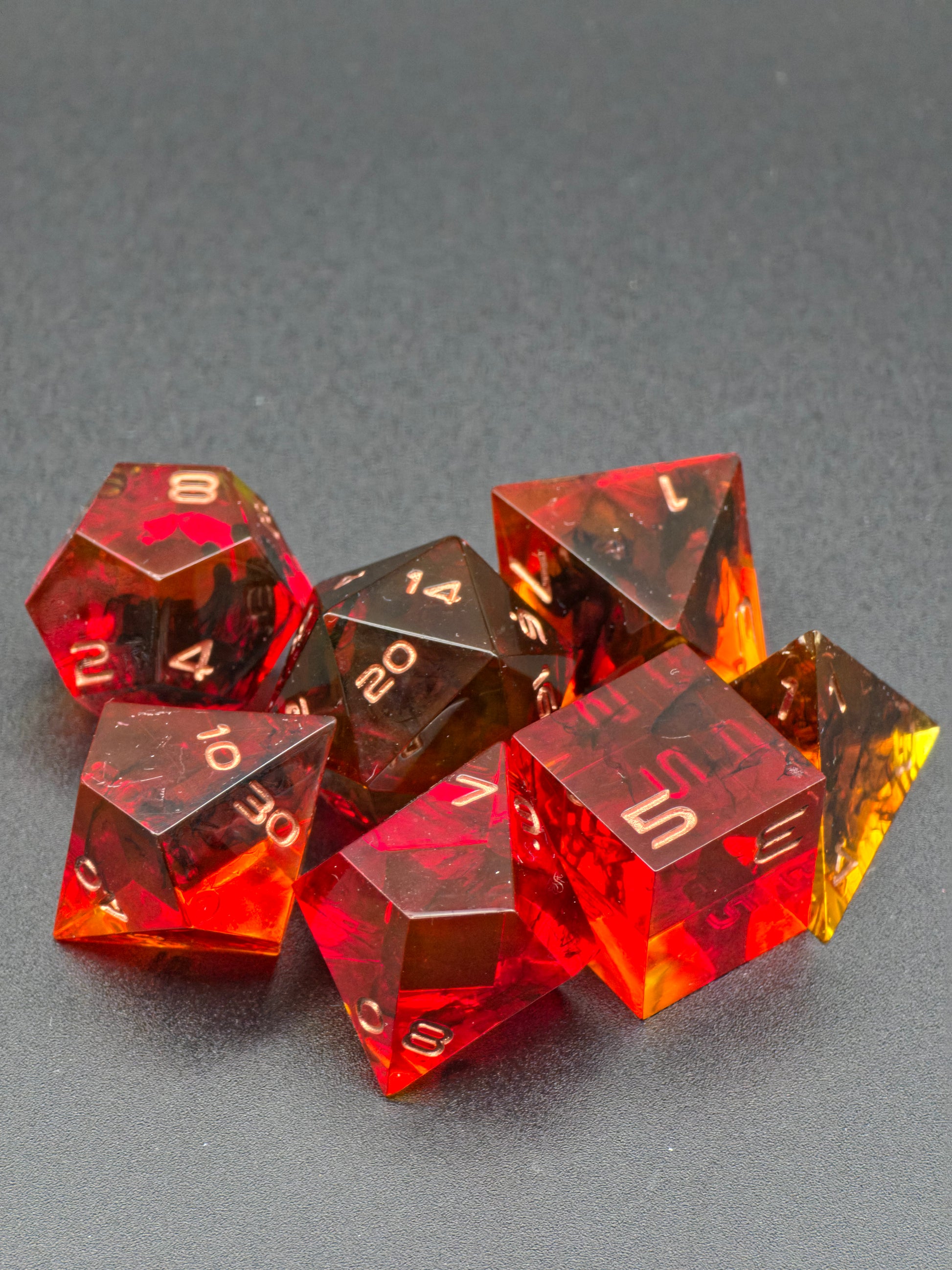 Polyedrisches „Crimson Emberflow“ Würfelset mit allen Würfelformen aus transparentem Resin.  
Polyhedral “Crimson Emberflow” dice set featuring all dice shapes made from transparent resin.