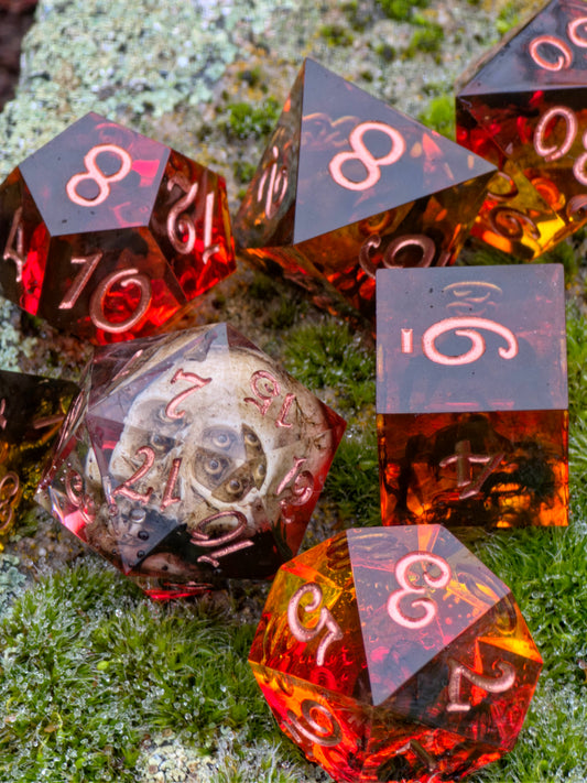 „Ember Relic“ – handgemachtes DnD Würfelset mit Schädel im D20, bernsteinrote Resinwürfel mit Kupferzahlen.  
“Ember Relic” – handmade DnD dice set featuring a skull inside the D20, amber-red resin dice with copper numbers.
