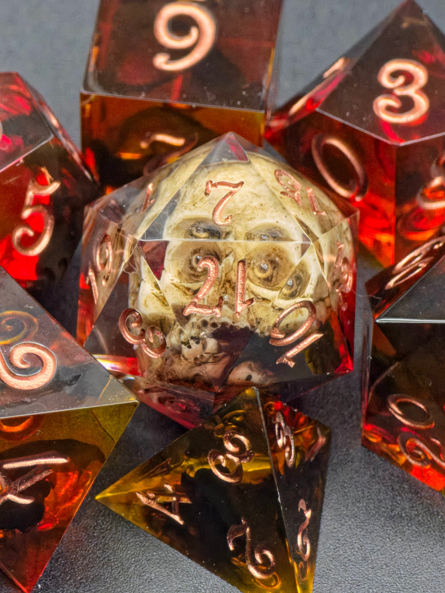 „Ember Relic“ Würfelset im natürlichen Licht, leuchtende Bernsteinfarben mit dunklem Fantasy-Charakter.  
“Ember Relic” dice set in natural light, glowing amber tones with a dark fantasy character.