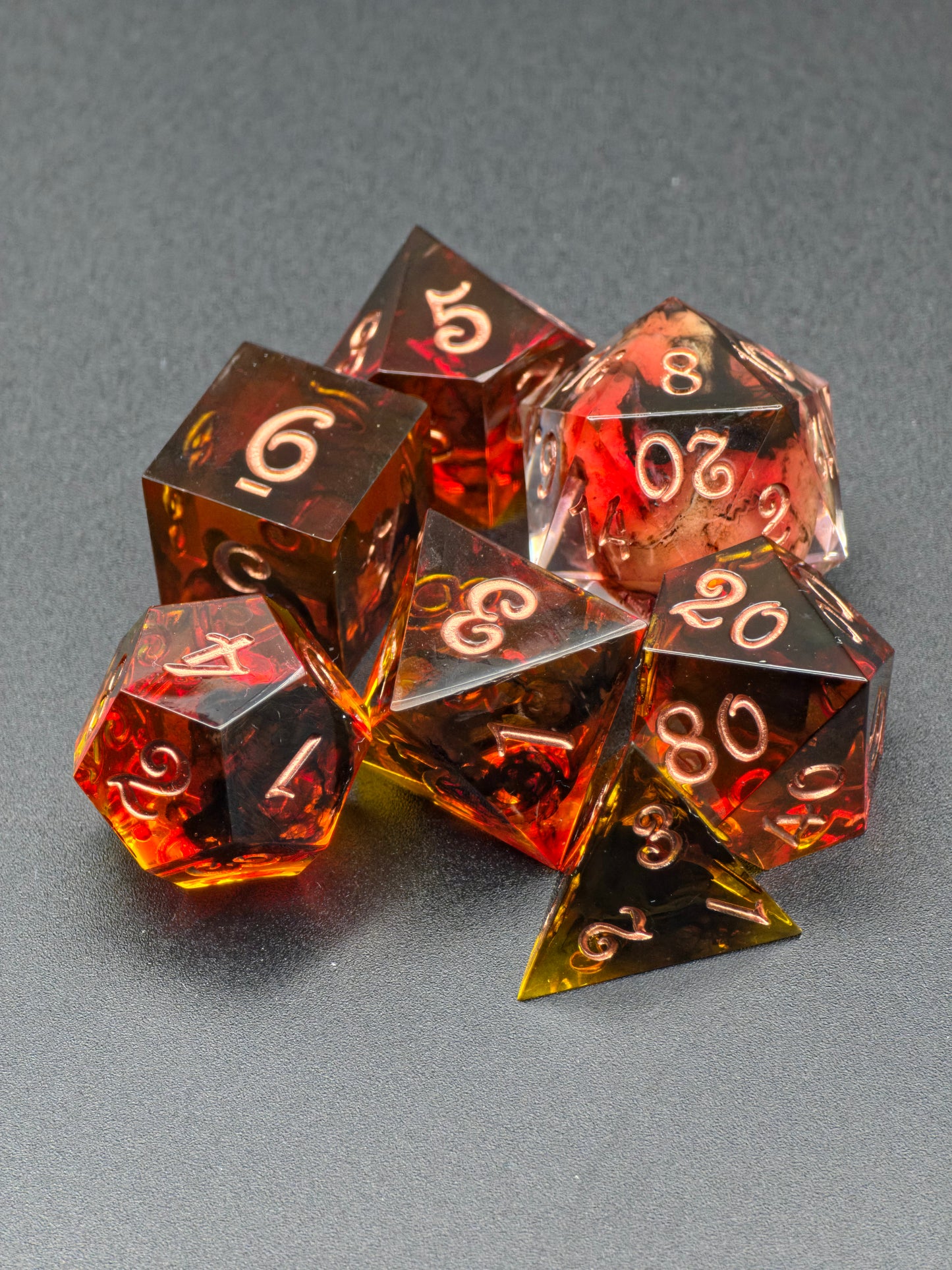 Nahaufnahme der bernsteinroten Resinwürfel mit Kupferzahlen im „Ember Relic“ DnD Würfelset.  
Close-up of amber-red resin dice with copper numbers in the “Ember Relic” DnD dice set.