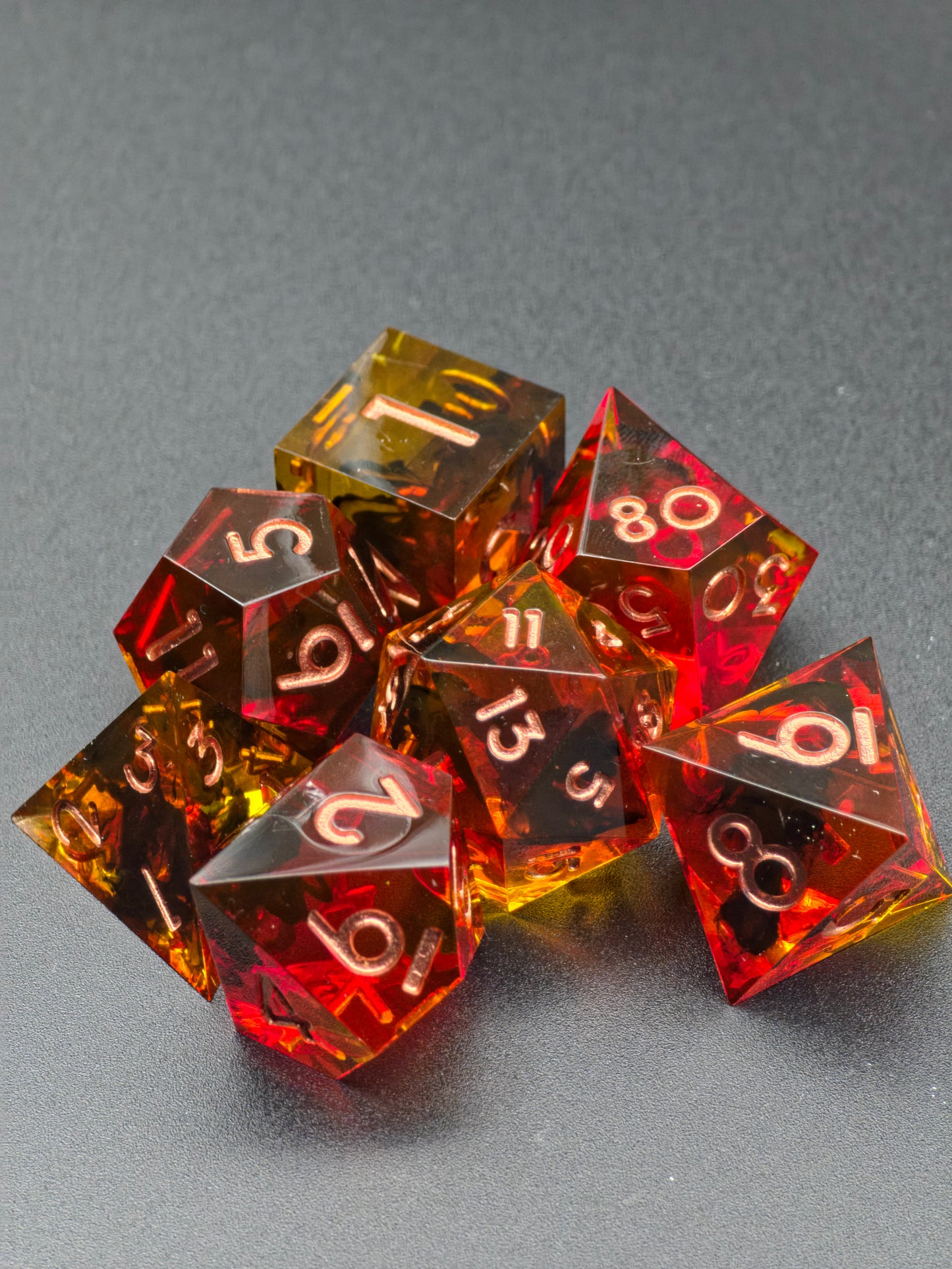 Polyedrisches Infernal Amberfall Würfelset mit sieben Würfelformen aus klarem Resin.  
Polyhedral Infernal Amberfall dice set featuring seven clear resin dice shapes.