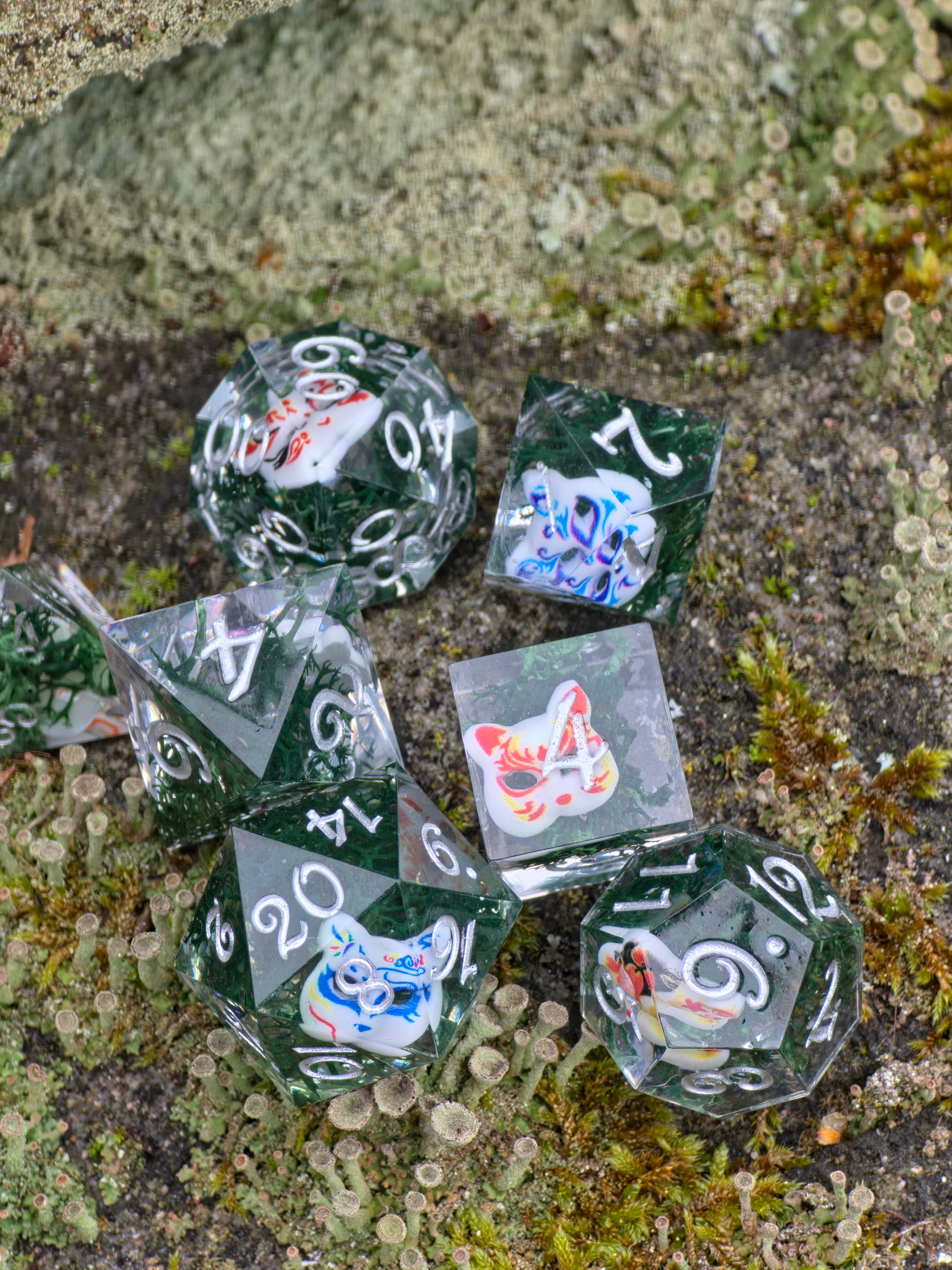 Detailaufnahme des „Kitsune Spirit Dice“ Würfelsets, klare Resinwürfel mit filigranen Kitsune-Masken Motiven.  
Close-up of the “Kitsune Spirit Dice” set, clear resin dice featuring delicate kitsune mask motifs.