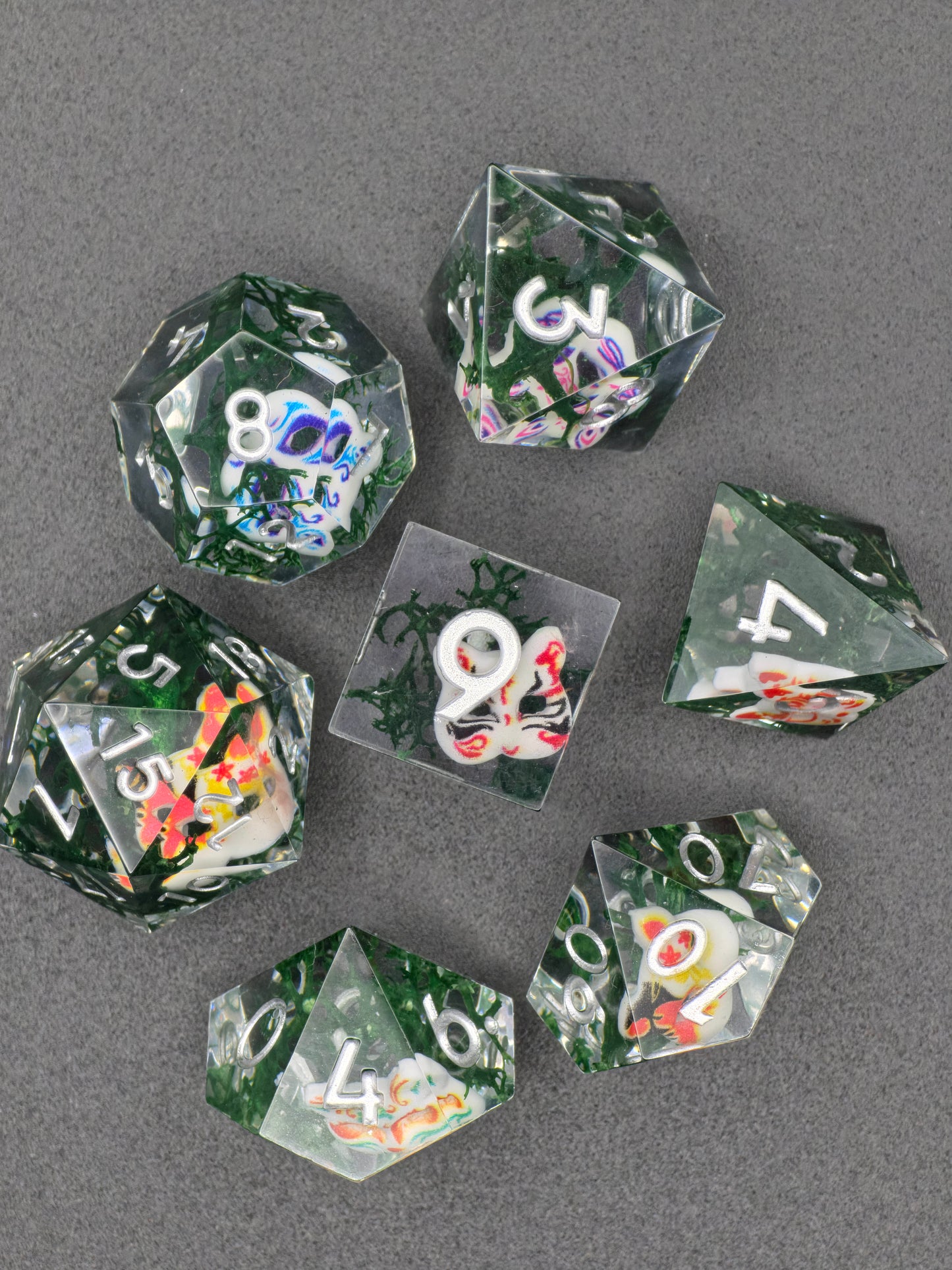 Detailaufnahme mit bunten japanischen Oni-Masken im transparenten Resin.  
Close-up showing colorful Japanese oni masks embedded in clear resin.