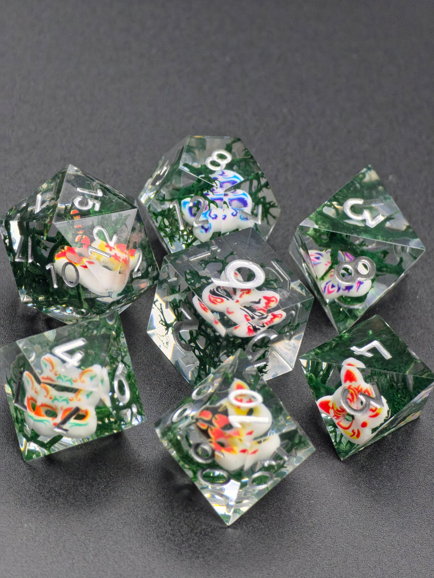 Handaufnahme des „Oni Curse Dice“ Sets mit dunklem Design und farbigen Maskenmotiven.  
Hand shot of the “Oni Curse Dice” set with dark design and colorful mask motifs.