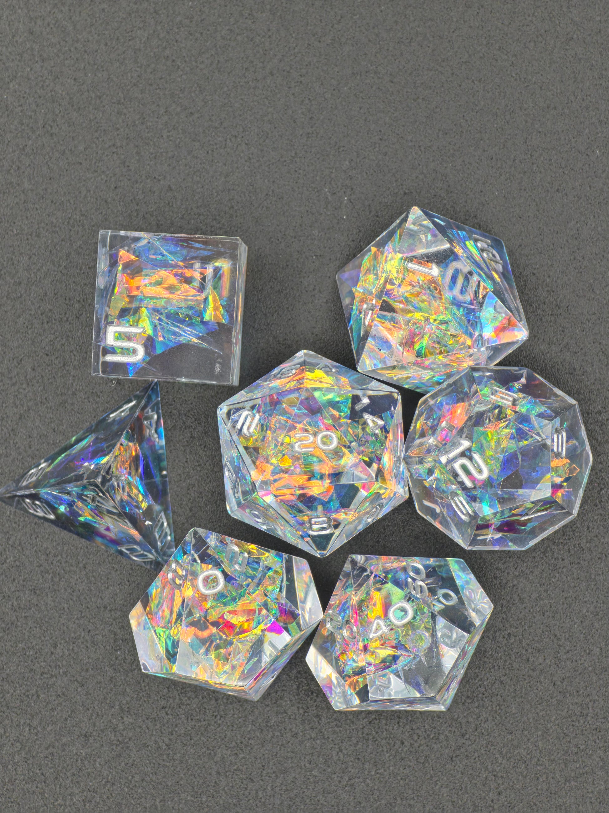 Detailaufnahme der holografischen Splitter im „Prismatic Aether“ Würfelset mit Regenbogenreflexionen. 
Close-up of holographic shards in the “Prismatic Aether” dice set with rainbow reflections.