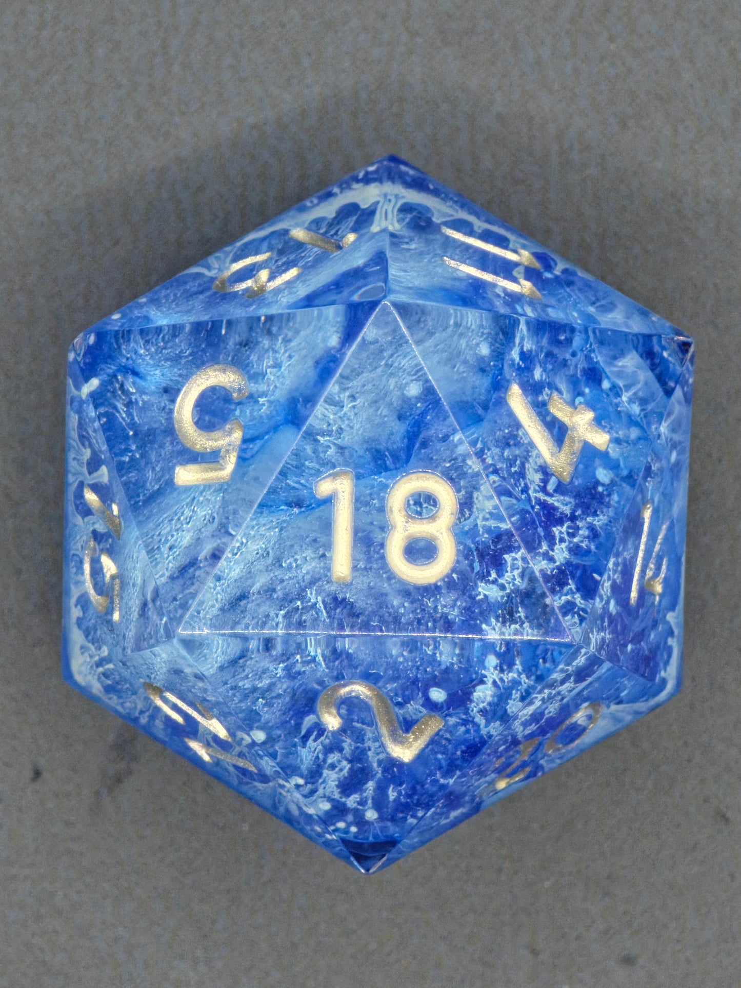 Handaufnahme des „Stormsealed Core“ – gefrorene Wirbel im blauen Harz, klar sichtbare goldene Zahlen.  
Hand shot of the “Stormsealed Core” – frozen swirls inside blue resin, gold numbers clearly visible.
