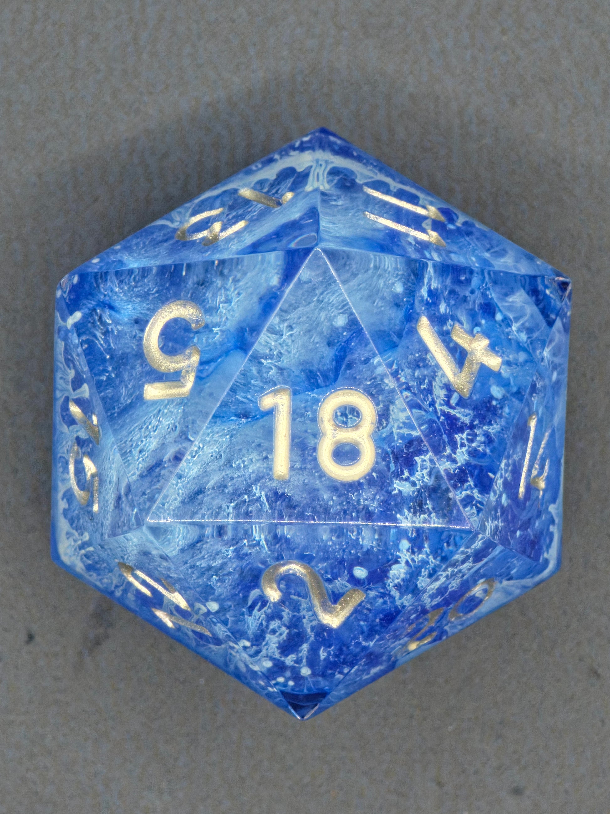 Handaufnahme des „Stormsealed Core“ – gefrorene Wirbel im blauen Harz, klar sichtbare goldene Zahlen.  
Hand shot of the “Stormsealed Core” – frozen swirls inside blue resin, gold numbers clearly visible.
