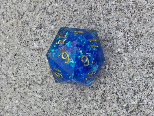 Handgemachter D20 „Arcane Energy“ – großer Liquid Core Würfel in tiefem Blau mit goldenem Schimmer.  
Handmade D20 “Arcane Energy” – large liquid core die in deep blue with golden shimmer.