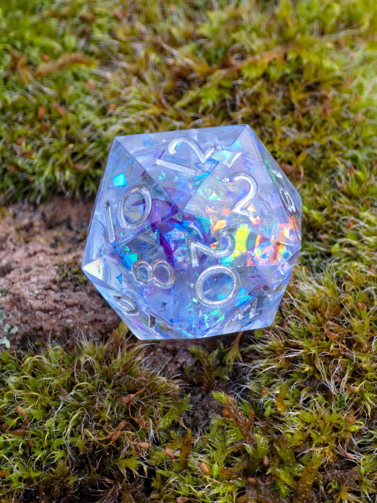 „Aurora Crystal“ D20 in der Hand – zeigt Größe, klare Gravuren und funkelnde Opalpartikel.  
“Aurora Crystal” D20 held in hand – showing size, crisp engravings and sparkling opal flakes.