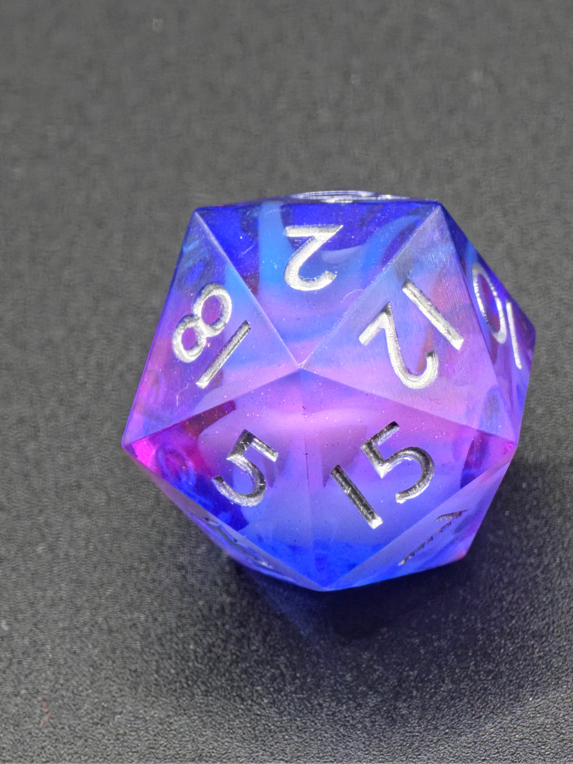 Handgemachter polyedrischer D20 „Cloud Blossom Nebula“ – blauer und lilafarbener Resinwürfel mit transparenter Tiefe.  
Handmade polyhedral D20 “Cloud Blossom Nebula” – blue and lilac resin die with transparent cosmic depth.