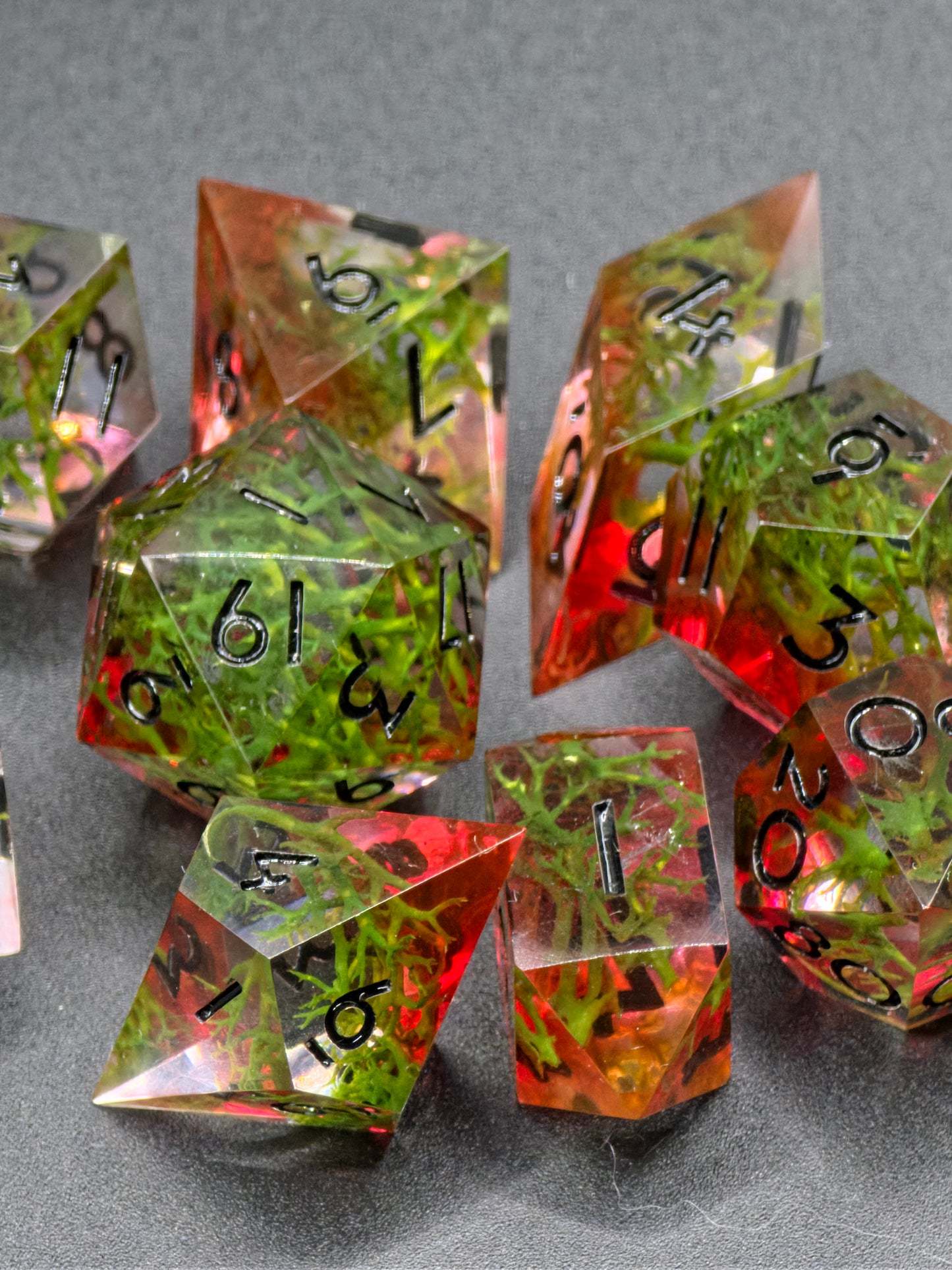 Handgemachtes polyedrisches Würfelset „Forest Ember“ – Resinwürfel mit Moos und rötlichem Glühen im Inneren.  
Handmade polyhedral dice set “Forest Ember” – resin dice with moss and reddish inner glow.