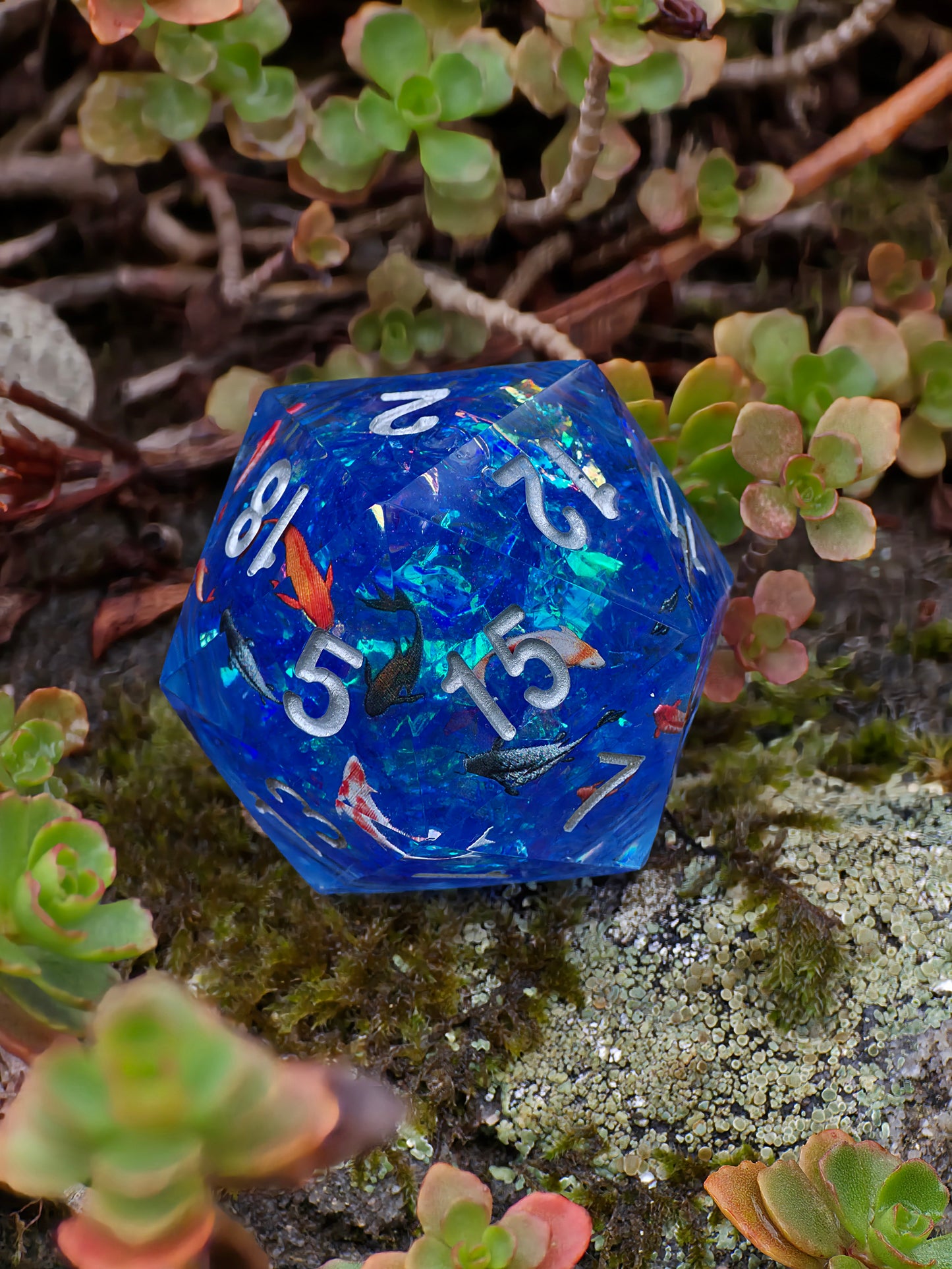 Handgemachter D20 „Koi Pond“ – großer Liquid Core Würfel mit schwimmenden Koi-Fischen in tiefblauem Harz.  
Handmade D20 “Koi Pond” – large liquid core die with floating koi fish in deep blue resin.