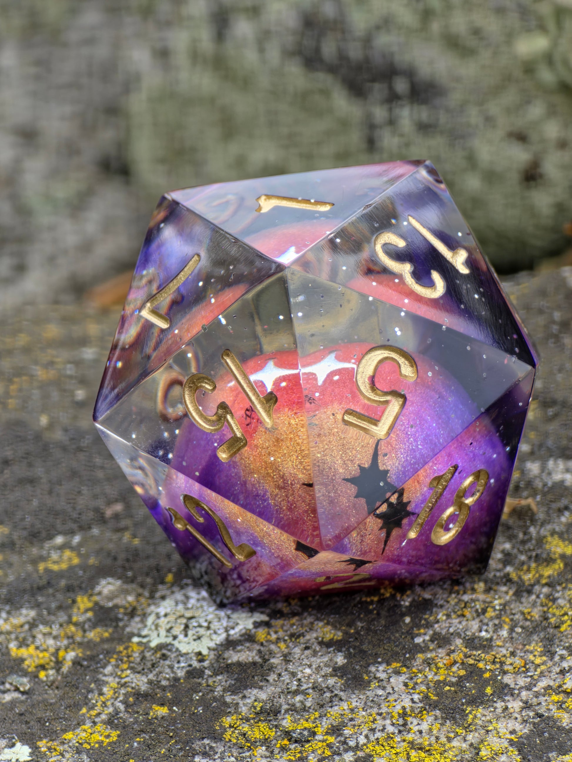 Handgemachter D20 „Planet Meteorite Galaxy“ – Resinwürfel in Violett-, Pink- und Goldtönen mit glitzernden Sternen.  
Handmade D20 “Planet Meteorite Galaxy” – resin die in violet, pink and gold hues with shimmering stars.